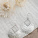 Pair of sterling silver hammered pear dangle earrings displayed on a white fabric with flowers in the background.

